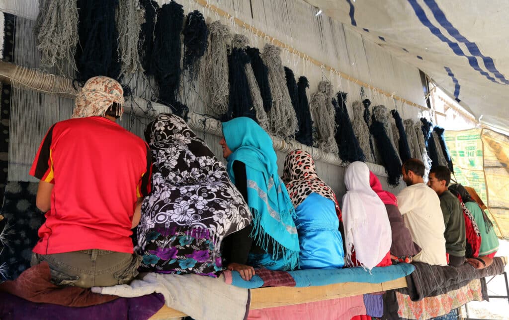 Afghan artisan rug weavers work on a large rug